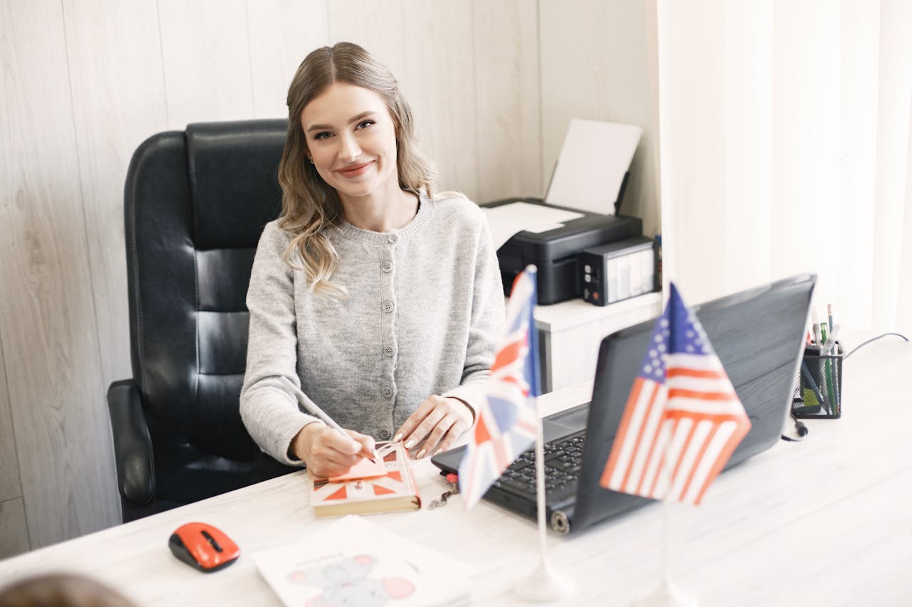 Smiling professional woman at desk with British and American flags, conveying international business.